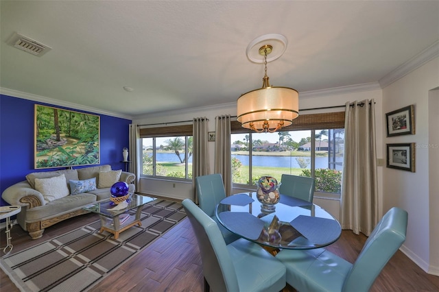 dining room featuring wood finished floors, visible vents, a water view, and ornamental molding