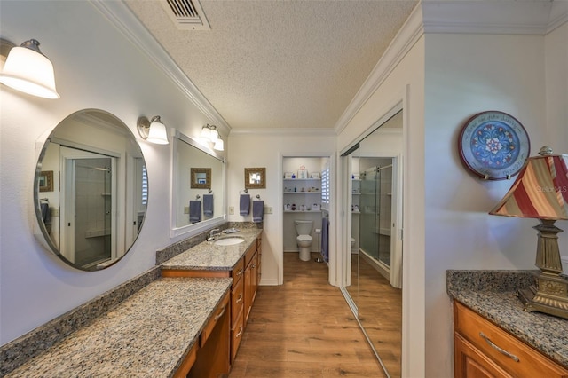 bathroom featuring toilet, ornamental molding, a stall shower, wood finished floors, and a textured ceiling