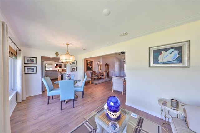 dining space with visible vents, a notable chandelier, crown molding, light wood finished floors, and baseboards