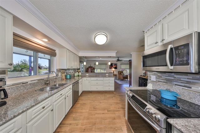 kitchen with light wood finished floors, a peninsula, a sink, appliances with stainless steel finishes, and tasteful backsplash