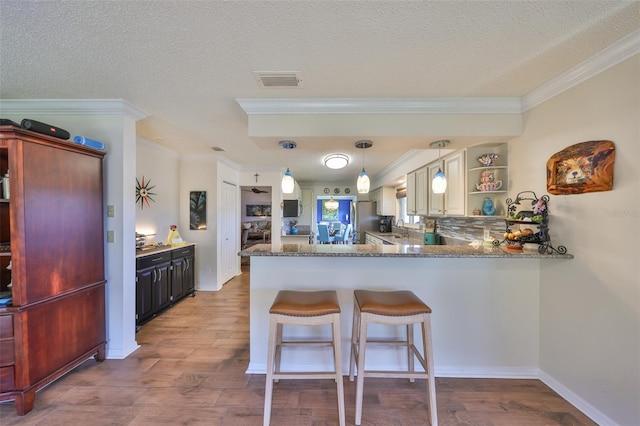 kitchen featuring a breakfast bar area, visible vents, open shelves, freestanding refrigerator, and a sink