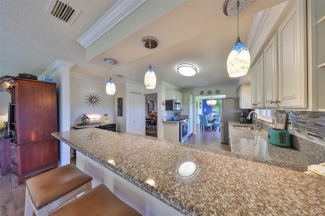 kitchen with visible vents, a peninsula, stainless steel appliances, crown molding, and backsplash