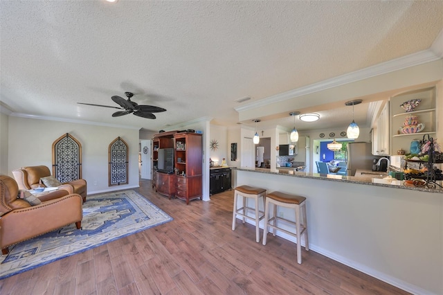 living area with a textured ceiling, ceiling fan, wood finished floors, and ornamental molding