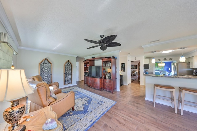 living area with a ceiling fan, wood finished floors, visible vents, a textured ceiling, and crown molding