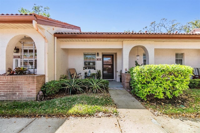 doorway to property with a porch, a tile roof, and stucco siding