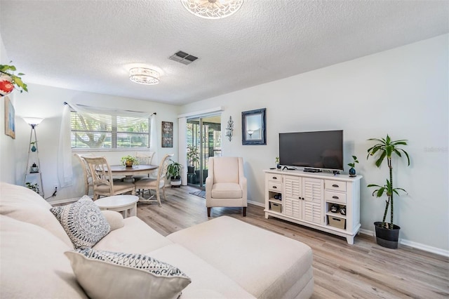 living room featuring visible vents, baseboards, a textured ceiling, and light wood-style flooring