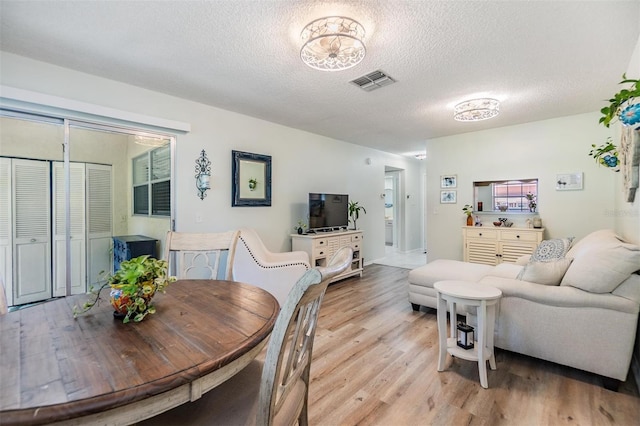 dining area with visible vents, light wood-style flooring, and a textured ceiling