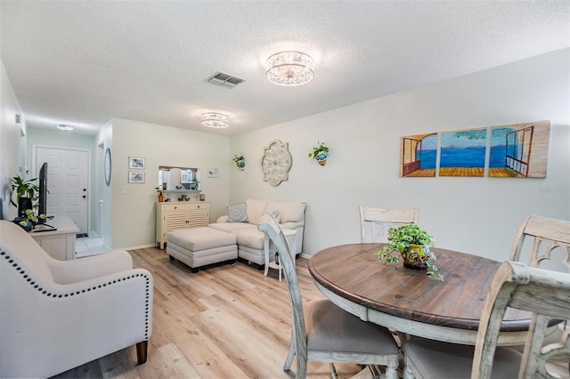 dining room featuring visible vents, baseboards, a textured ceiling, and light wood-style flooring