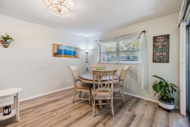 dining room with baseboards, a textured ceiling, and light wood-style floors