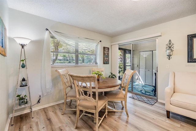 dining area with light wood finished floors, a textured ceiling, and baseboards