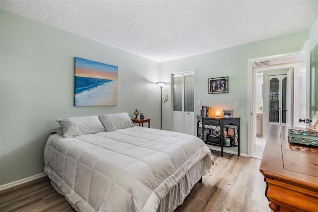 bedroom featuring visible vents, baseboards, light wood-type flooring, and a textured ceiling