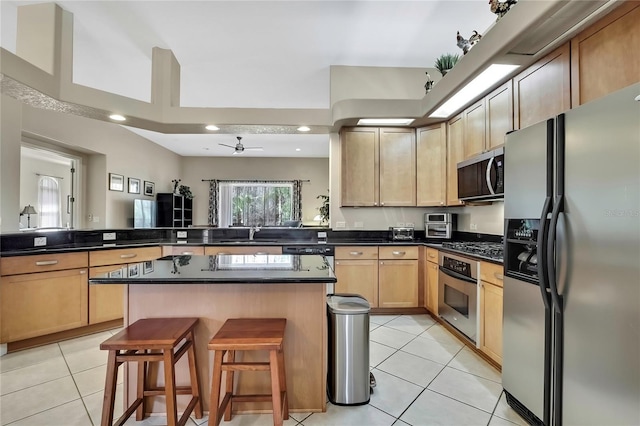 kitchen featuring a breakfast bar, light brown cabinetry, stainless steel appliances, light tile patterned floors, and ceiling fan