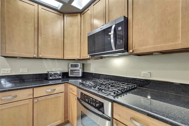 kitchen featuring light brown cabinets, dark stone countertops, appliances with stainless steel finishes, and a textured wall