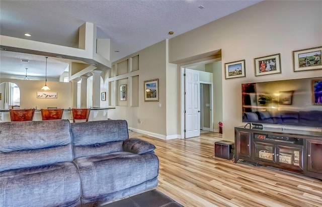 living area with baseboards, a textured ceiling, wood finished floors, and ornate columns