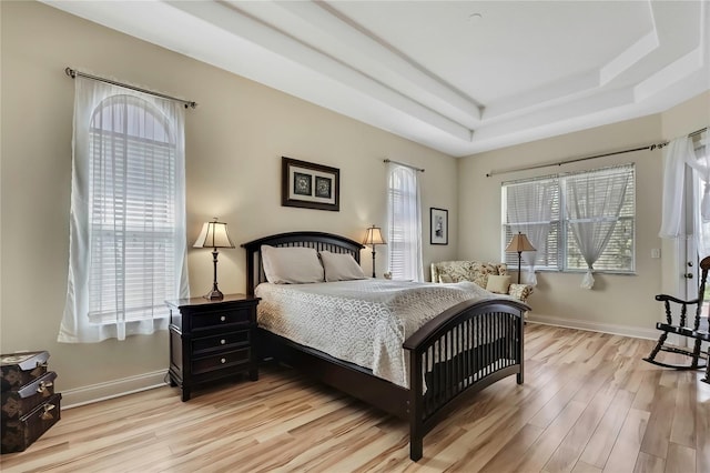 bedroom featuring a tray ceiling, baseboards, and light wood finished floors