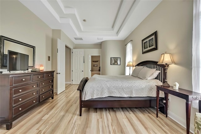 bedroom featuring visible vents, baseboards, light wood-style floors, and a tray ceiling