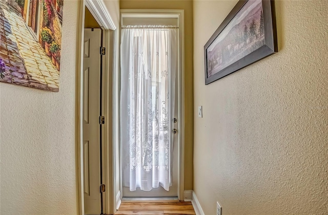 doorway to outside featuring light wood-type flooring, plenty of natural light, baseboards, and a textured wall