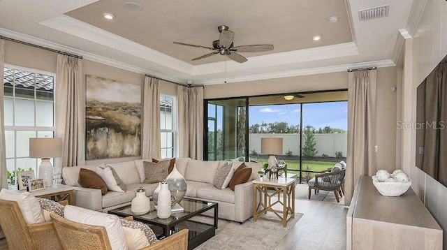 living area with visible vents, light wood-style flooring, a raised ceiling, and a ceiling fan