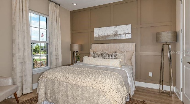 bedroom featuring multiple windows, wood finished floors, and a decorative wall