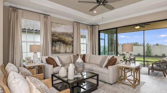 living area featuring plenty of natural light, light wood-style flooring, crown molding, and a tray ceiling