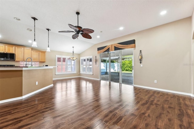 unfurnished living room featuring a healthy amount of sunlight, dark wood-style flooring, a ceiling fan, and vaulted ceiling