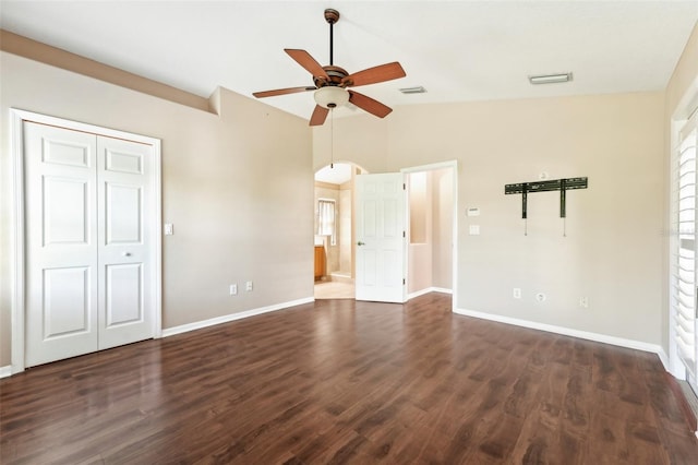 unfurnished bedroom featuring baseboards, visible vents, arched walkways, dark wood-type flooring, and vaulted ceiling