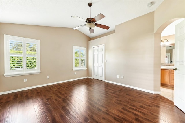 unfurnished bedroom with baseboards, arched walkways, lofted ceiling, and hardwood / wood-style flooring