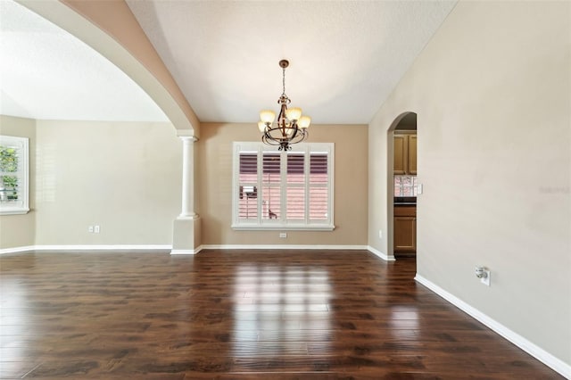 interior space with a notable chandelier, lofted ceiling, dark wood-style floors, arched walkways, and baseboards