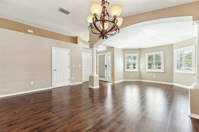 spare room with dark wood finished floors, a notable chandelier, decorative columns, and visible vents