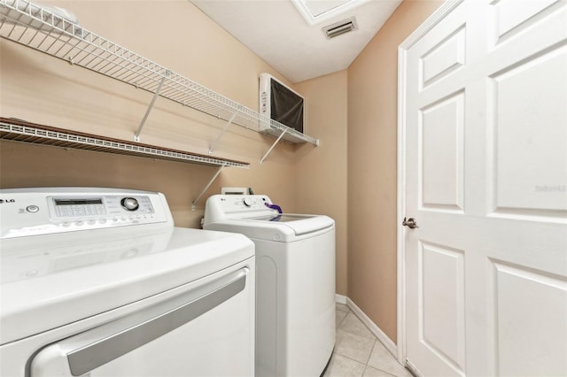 clothes washing area featuring visible vents, baseboards, laundry area, light tile patterned flooring, and washing machine and dryer