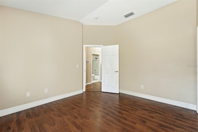 empty room featuring visible vents, baseboards, dark wood finished floors, and vaulted ceiling