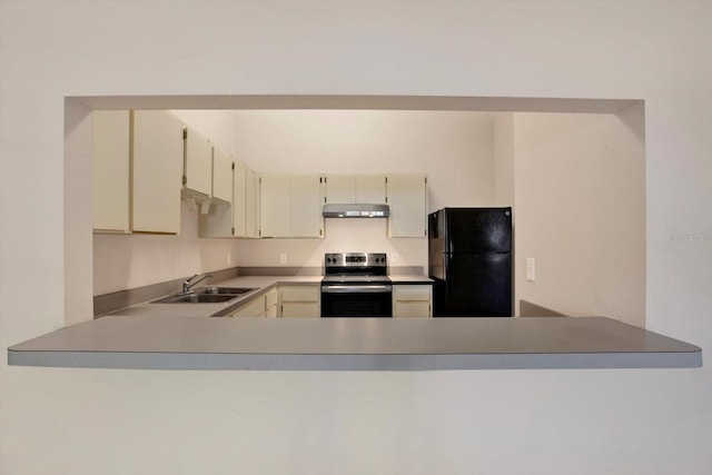 kitchen with cream cabinetry, a sink, under cabinet range hood, freestanding refrigerator, and stainless steel range with electric cooktop