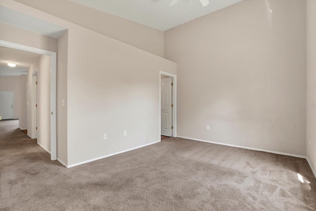 carpeted spare room featuring ceiling fan, a high ceiling, and baseboards