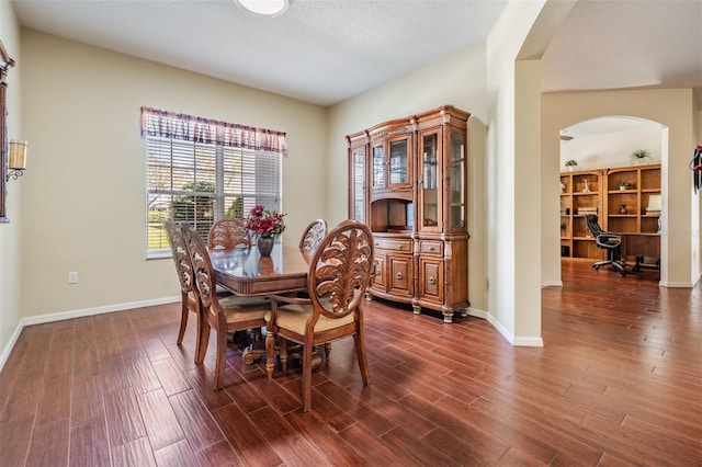 dining space featuring dark wood-style floors, arched walkways, and baseboards