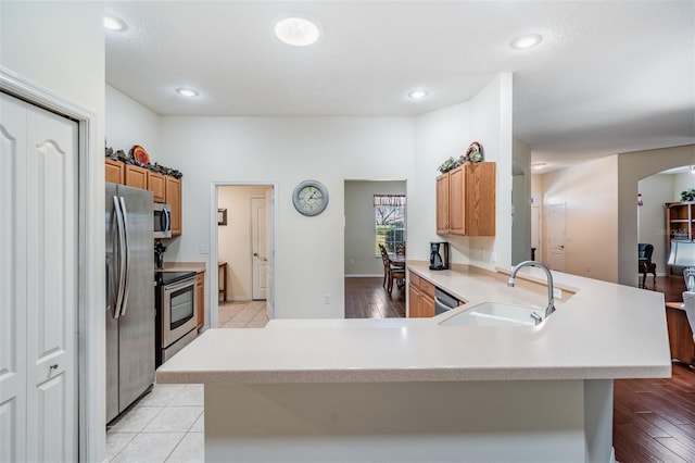 kitchen featuring a peninsula, arched walkways, stainless steel appliances, a sink, and light countertops