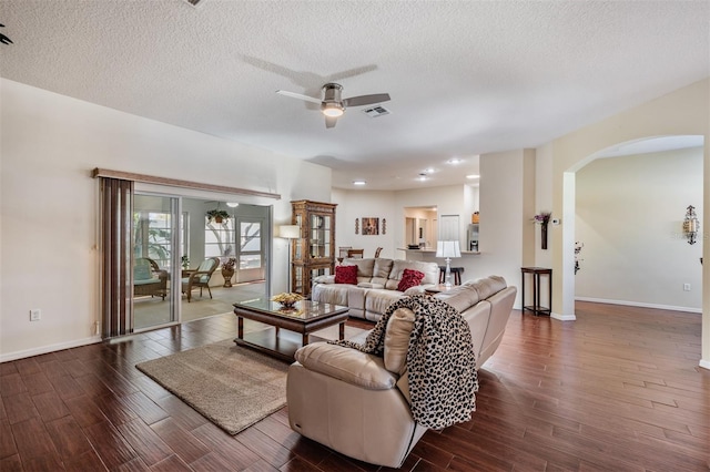 living room featuring arched walkways, baseboards, dark wood-type flooring, and ceiling fan