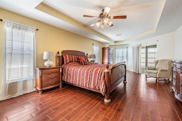 bedroom with wood finish floors, a raised ceiling, a textured ceiling, and a ceiling fan