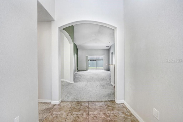 corridor with arched walkways, tile patterned flooring, baseboards, and carpet floors