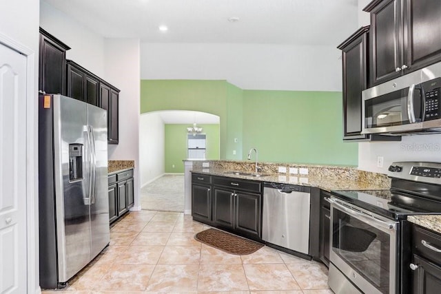 kitchen with light stone countertops, a peninsula, arched walkways, stainless steel appliances, and a sink