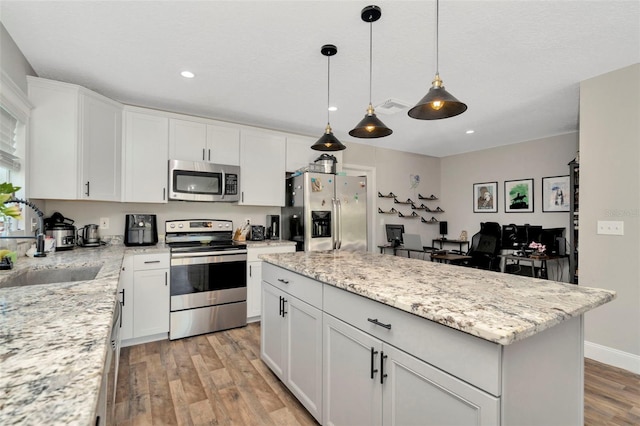 kitchen featuring visible vents, a center island, stainless steel appliances, light wood-style floors, and white cabinets