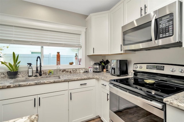 kitchen with a sink, stainless steel appliances, light stone counters, and white cabinetry