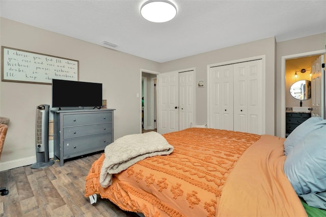 bedroom featuring visible vents, multiple closets, ensuite bathroom, wood finished floors, and baseboards