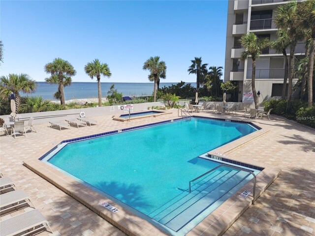 pool with a patio, a community hot tub, and a water view