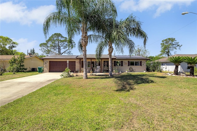 ranch-style home with a front lawn, an attached garage, solar panels, and driveway