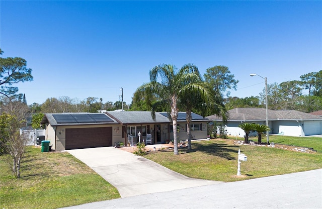 single story home featuring covered porch, a front lawn, concrete driveway, a garage, and roof mounted solar panels