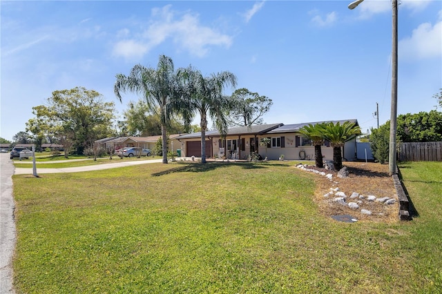 view of front of property featuring a front yard, fence, driveway, solar panels, and a garage