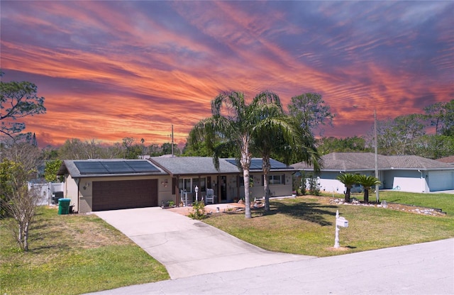 ranch-style house featuring roof mounted solar panels, a front lawn, concrete driveway, an attached garage, and covered porch