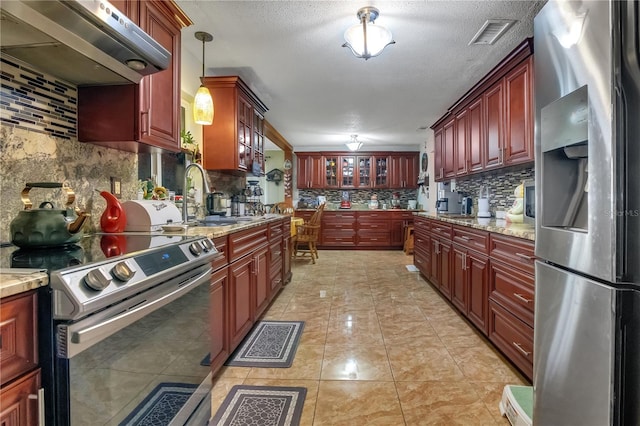kitchen with under cabinet range hood, stainless steel appliances, visible vents, a sink, and decorative backsplash