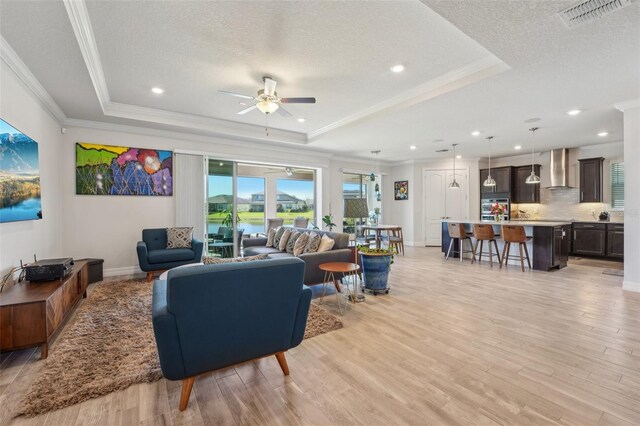 living area featuring visible vents, light wood-style floors, and a tray ceiling