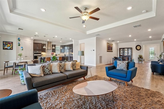 living room with visible vents, ornamental molding, light wood-style flooring, baseboards, and a raised ceiling